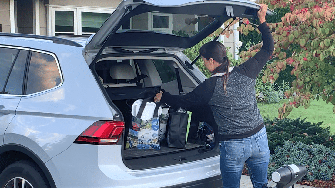 Woman putting re-usable bags with recycling material in trunk of car