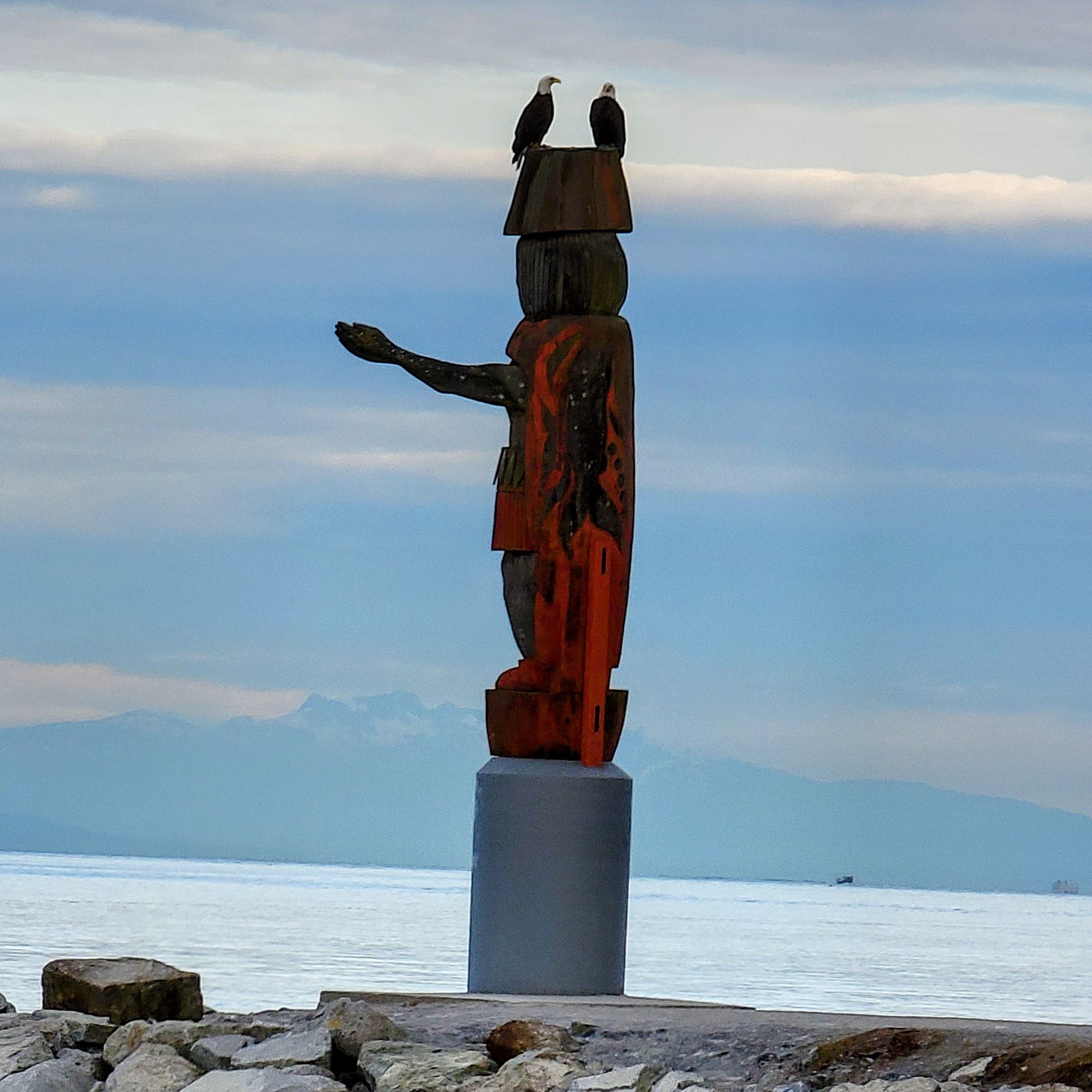 Photo of the Welcoming Figure from behind showing the ocean and mountains of Squamish Nation in the background
